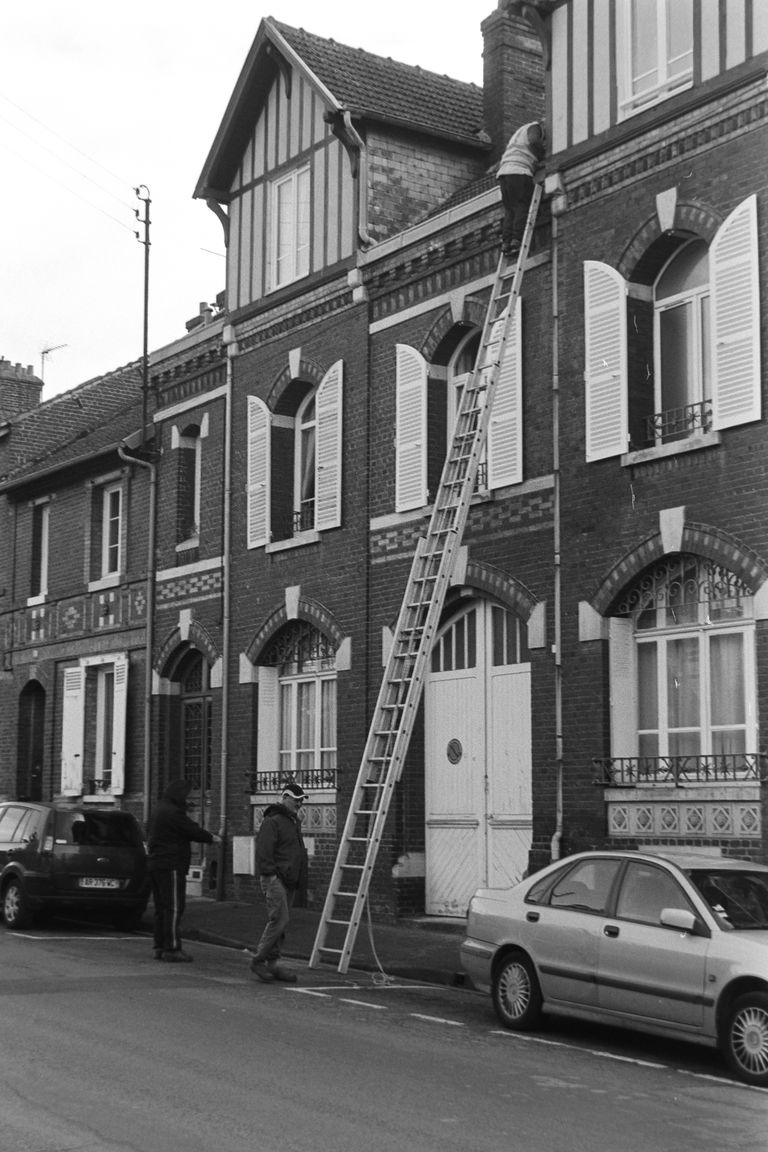 A black and white photo of traditional brick apartments and a man on a ladder in Compiègne, France.
